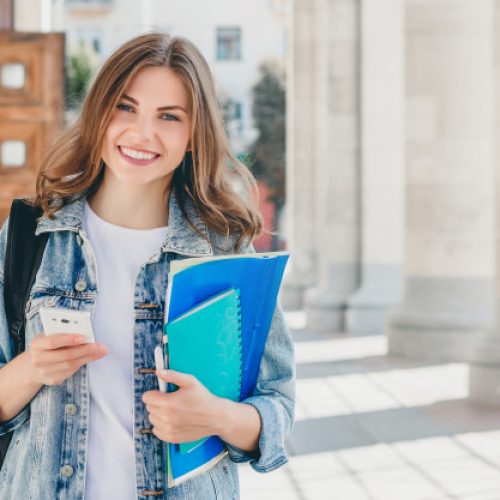 young-girl-student-smiling-against-university-cute-girl-student-holds-folders-notebooks-mobile-phone-hands-learning-education_101969-618